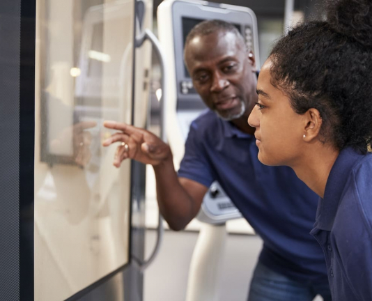 Engineer Showing Apprentice How To Use CNC Tool Making Machine