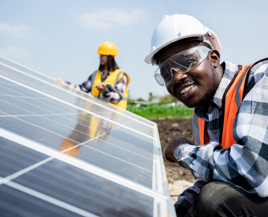 Two workers technicians installing heavy solar photo voltaic panels to high steel platform in corn field. Photovoltaic module idea for clean energy. Green energy concept