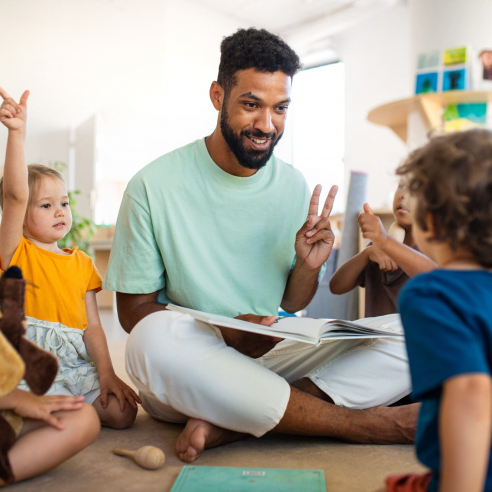 Group of small nursery school children with man teacher sitting on floor indoors in classroom, having lesson.